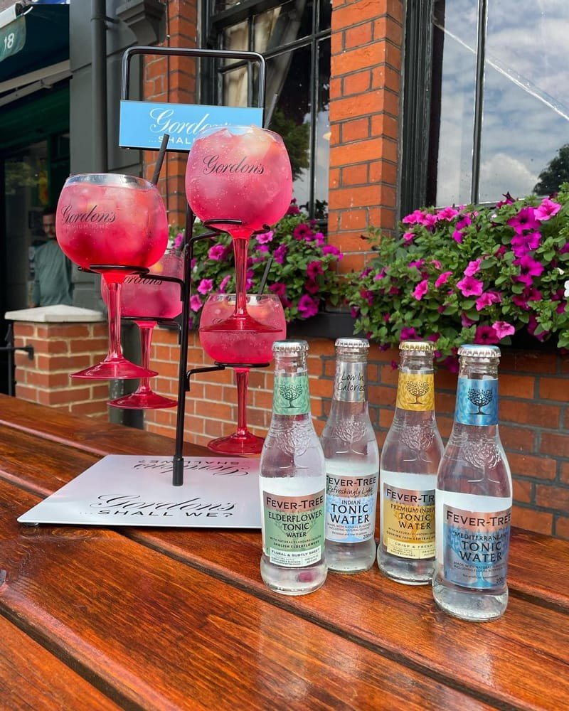 Pink cocktails in glasses on a stand beside tonic bottles, on the terrace