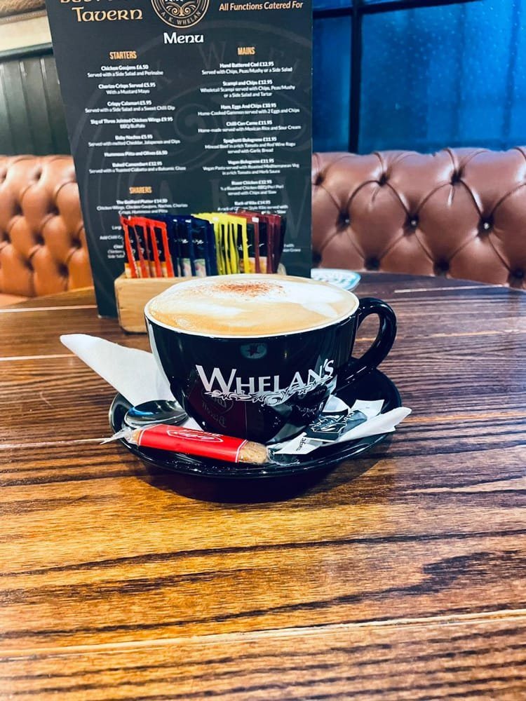 A cappuccino in a Whelan's cup on a wooden table, the menu propped behind