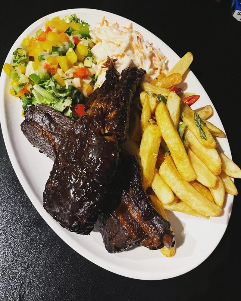 A plate of glazed ribs with chips, coleslaw and salad