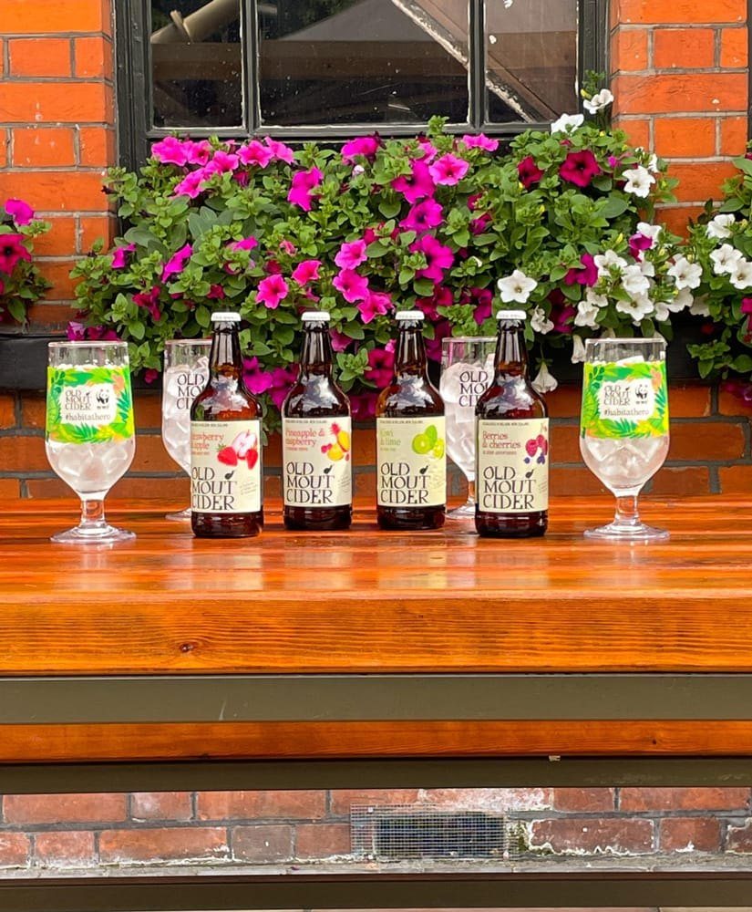 Bottles of cider and glasses on the front ledge, under a window box of pink petunias