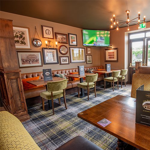 The dining area: green velvet chairs at wooden tables set with menus, a leather banquette with orange cushions and a wall of framed prints