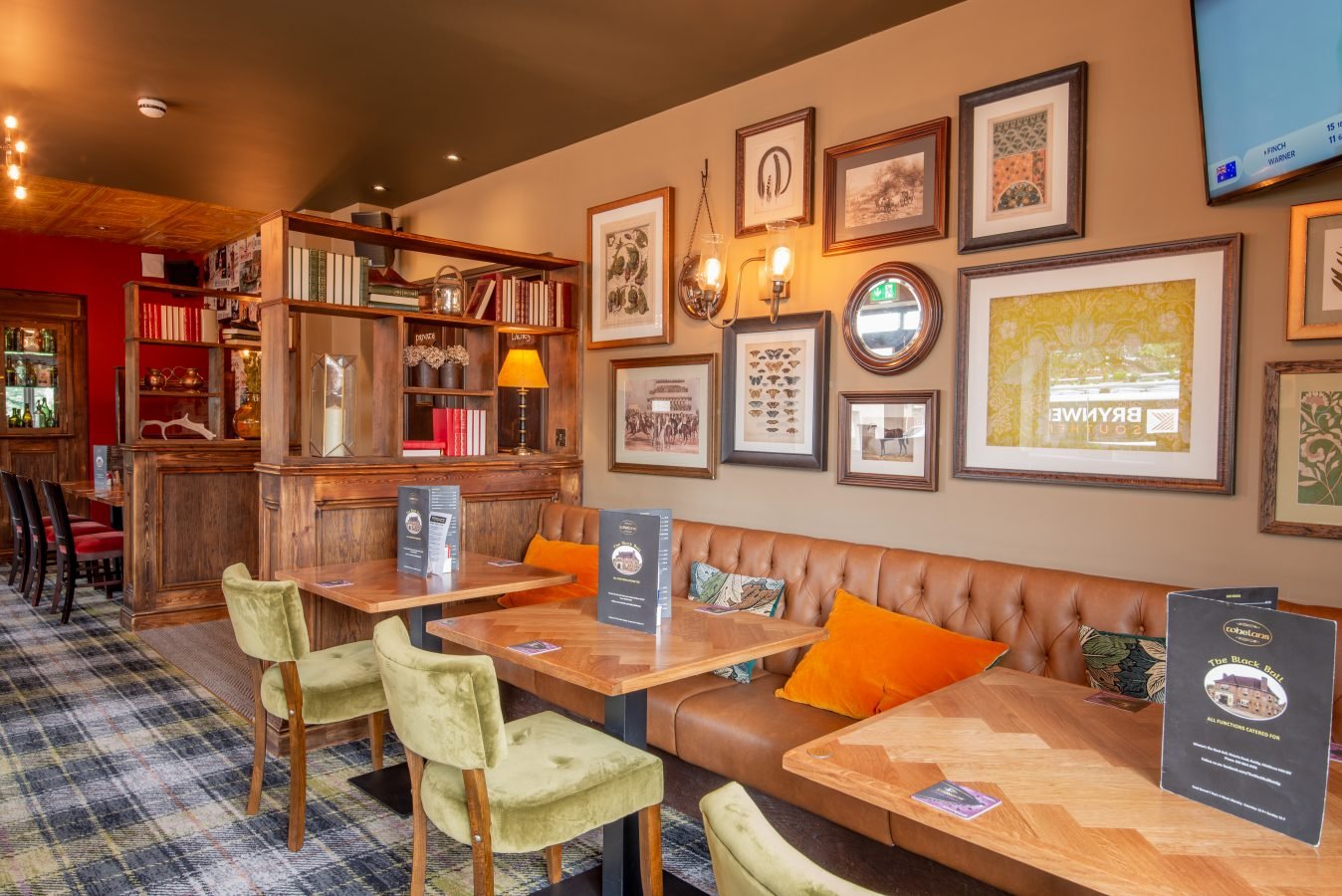 A lounge area at The Black Bull: gallery of framed prints, orange cushions on a leather banquette, a screen in the corner