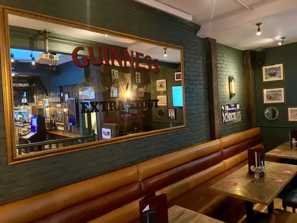 A gold-framed Guinness Extra Stout mirror above a leather booth, green brick walls behind