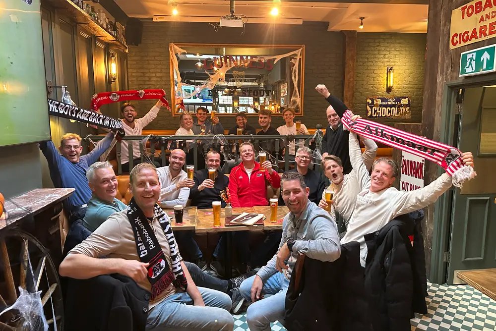 A group of fans celebrating with scarves raised, a Guinness mirror on the wall behind