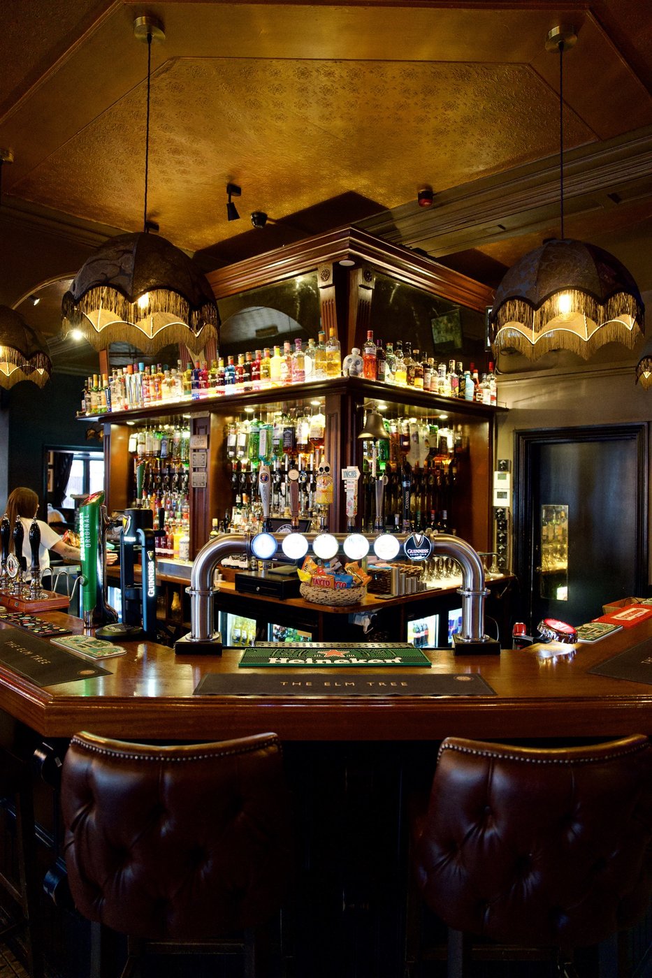 The bar at The Elm Tree: fringed pendant lampshades over a full spirits gantry and the beer taps