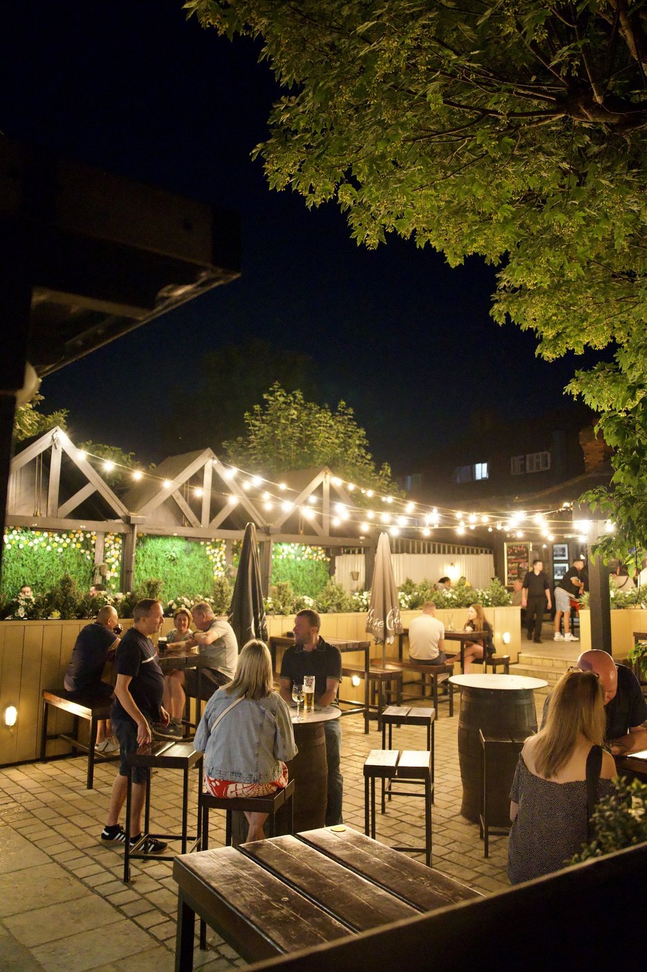 The beer garden at night: high tables and stools under string lighting