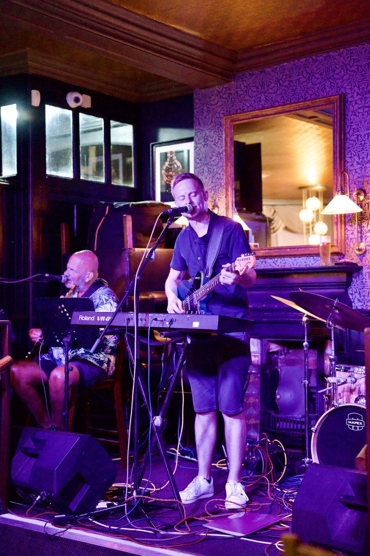 A live act performing on guitar and keyboard under purple stage lighting
