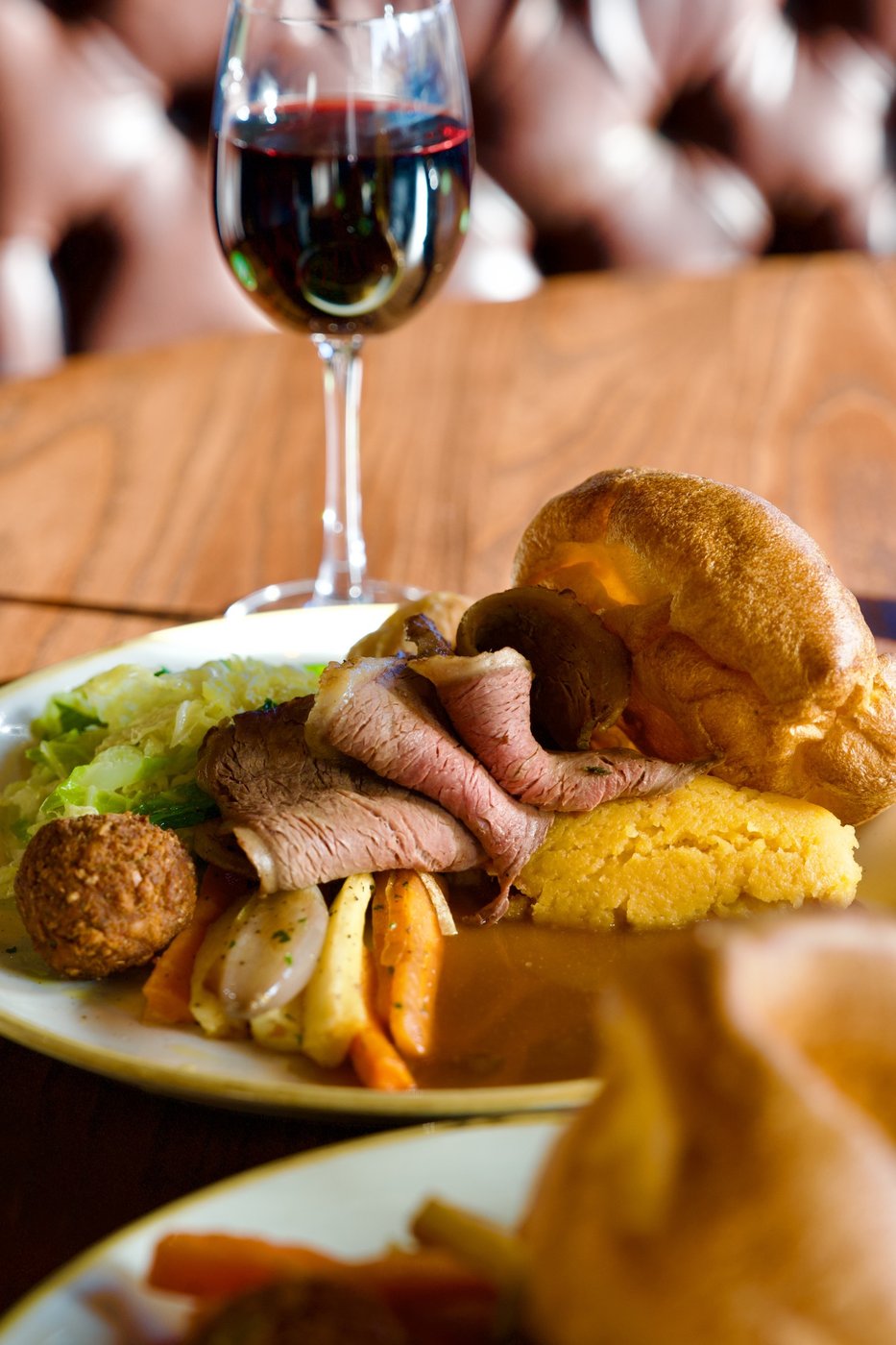 A roast dinner: beef with a Yorkshire pudding, roast potatoes and vegetables, beside a glass of red wine