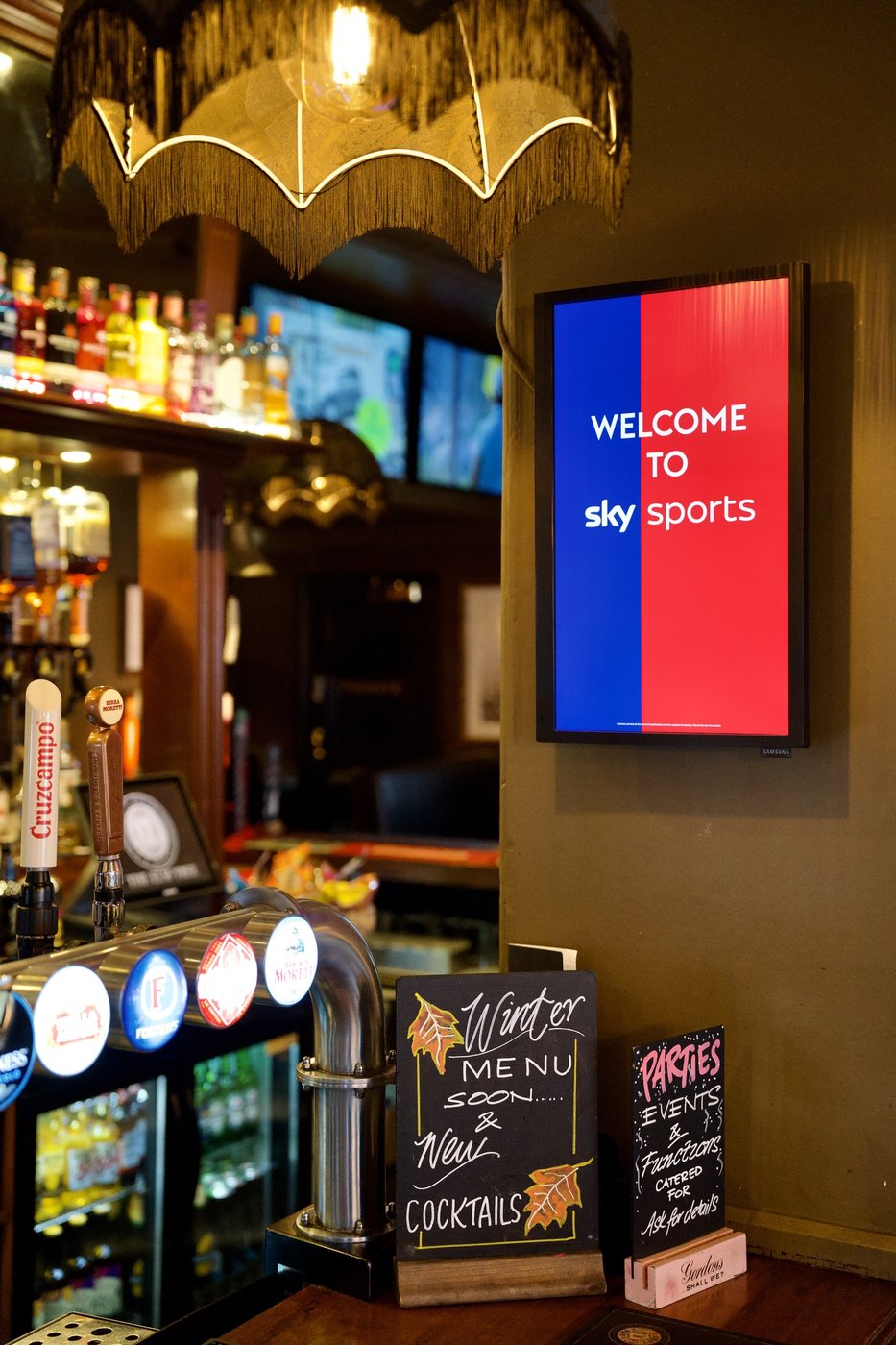 A Sky Sports screen above the bar, with the drinks fridges and a chalkboard menu below