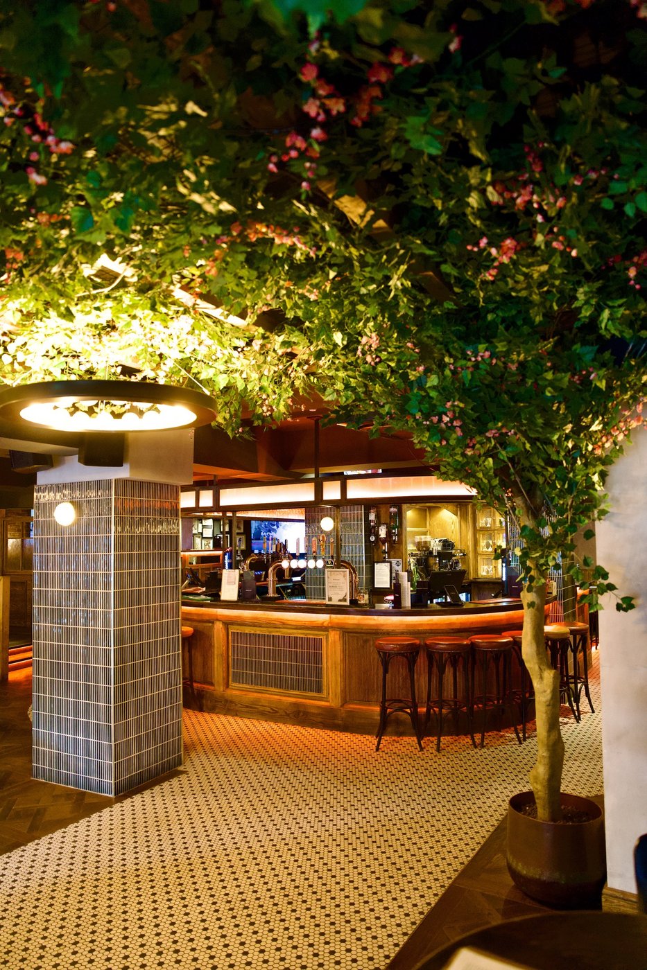 The bar beneath a canopy of foliage and blossom, a ring light overhead and tiled columns either side