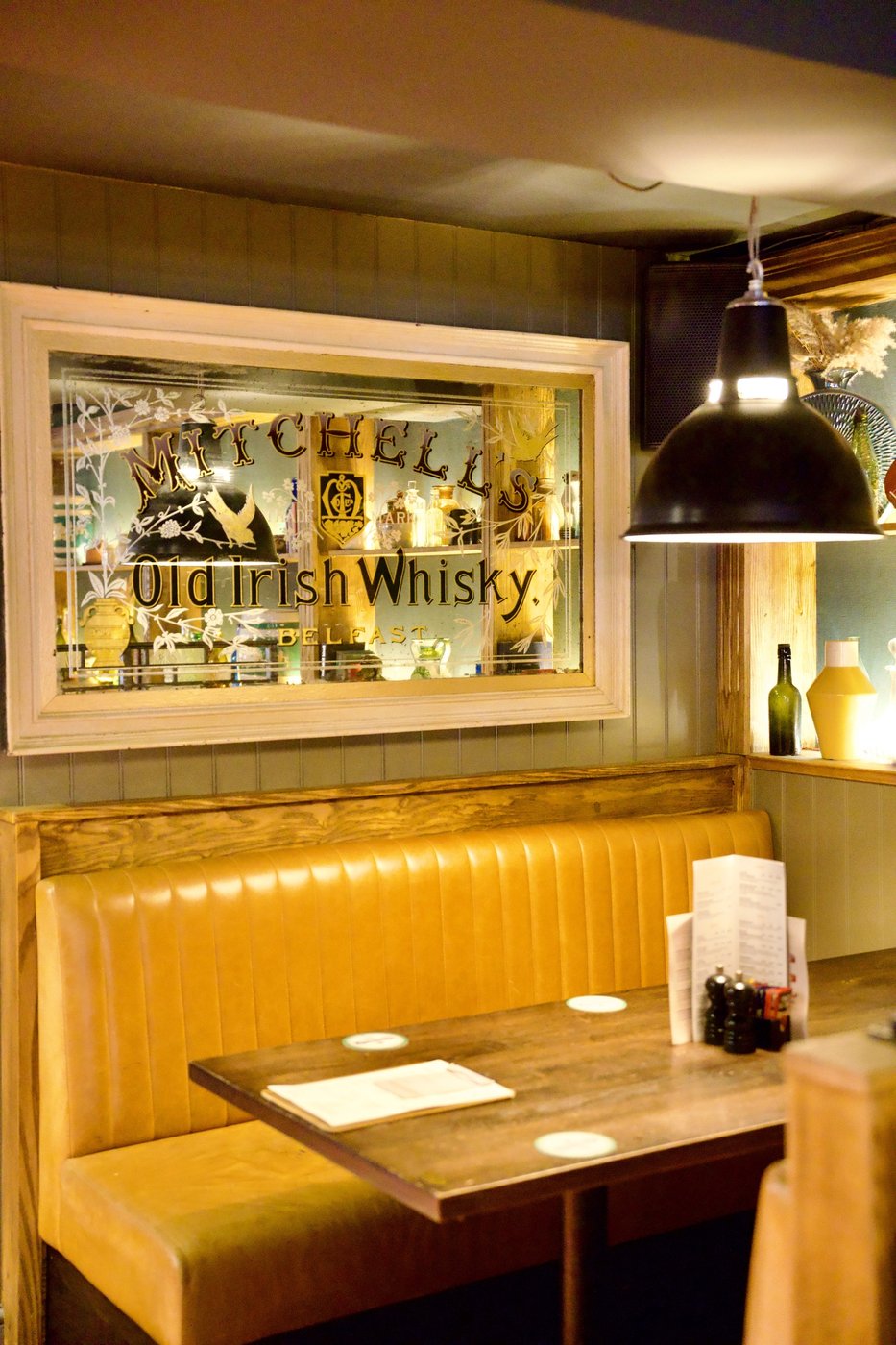 A booth with mustard banquette seating beneath an Old Irish Whisky mirror