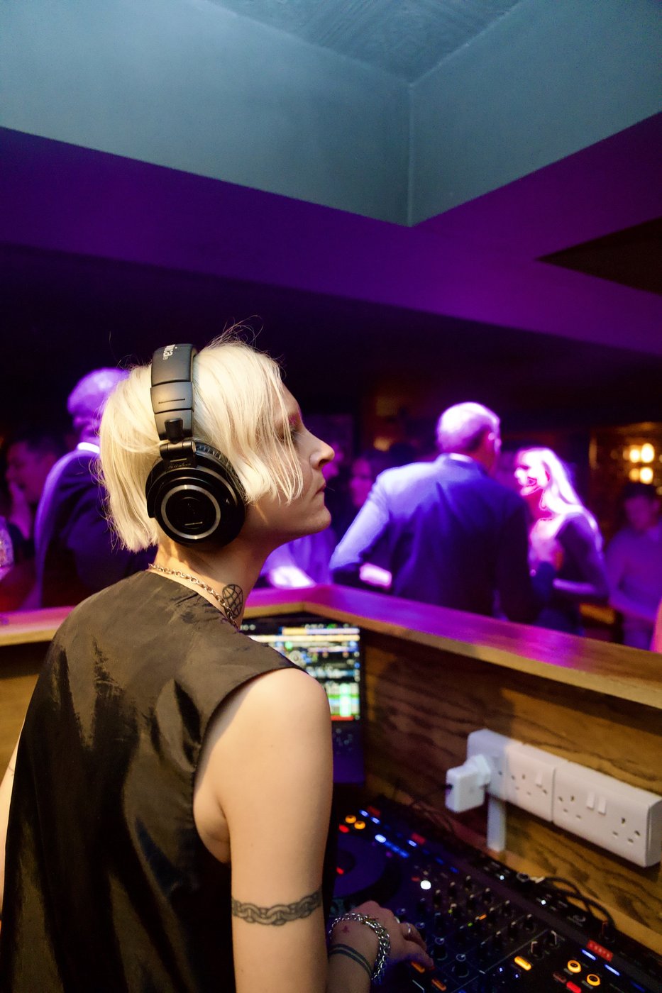 A DJ in headphones behind the decks under purple lighting