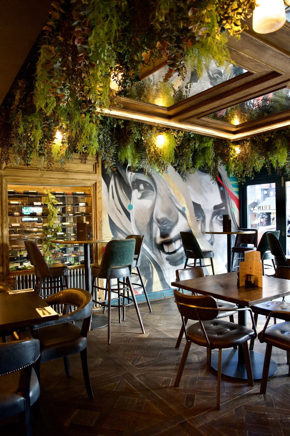 The dining area beneath hanging greenery, a large painted face mural along the wall