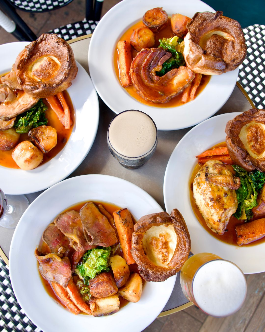 An overhead spread of Sunday roasts: Yorkshire puddings, roast potatoes and greens, with a pint