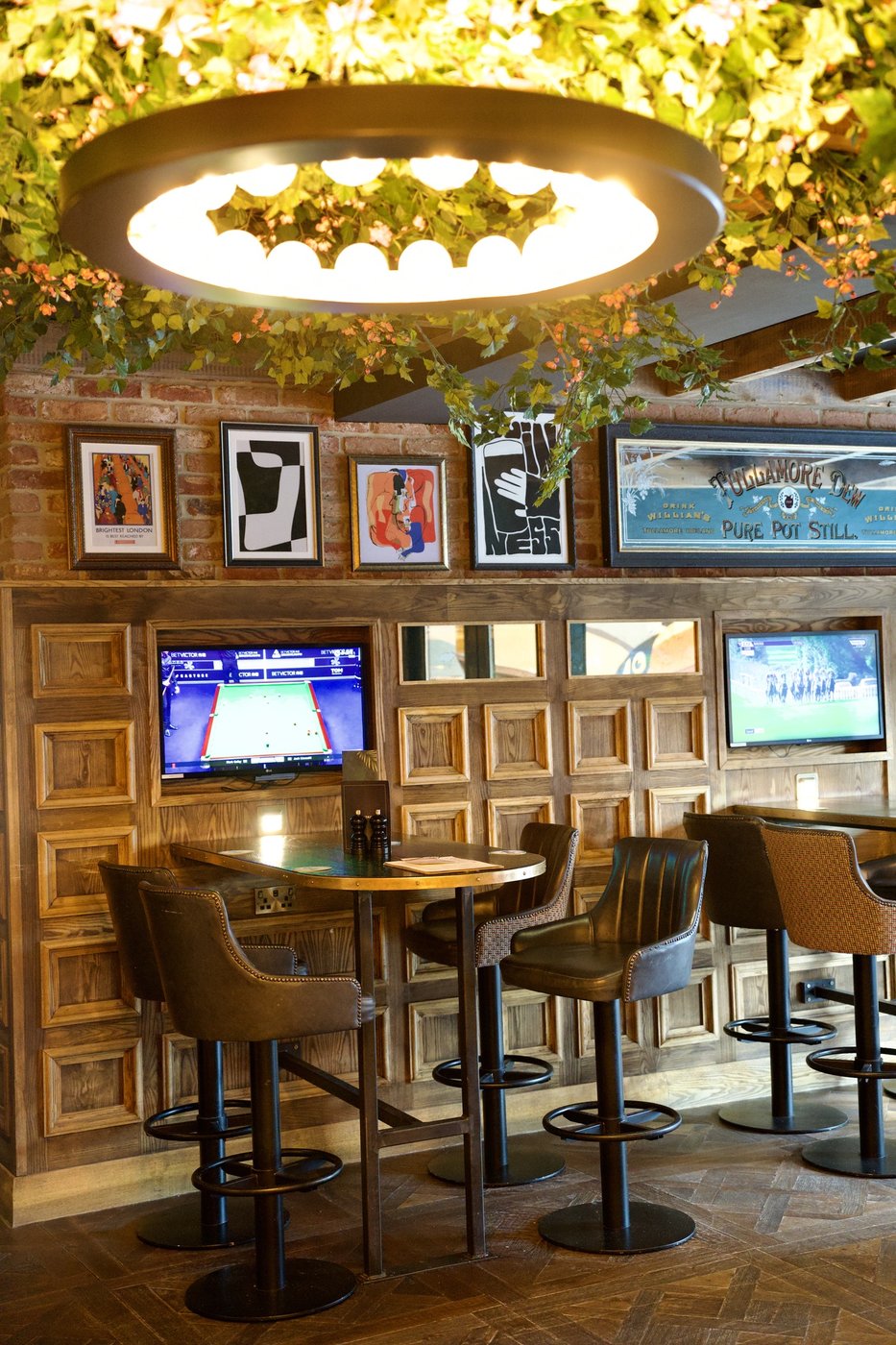 A wall of screens showing sport above panelled booth seating