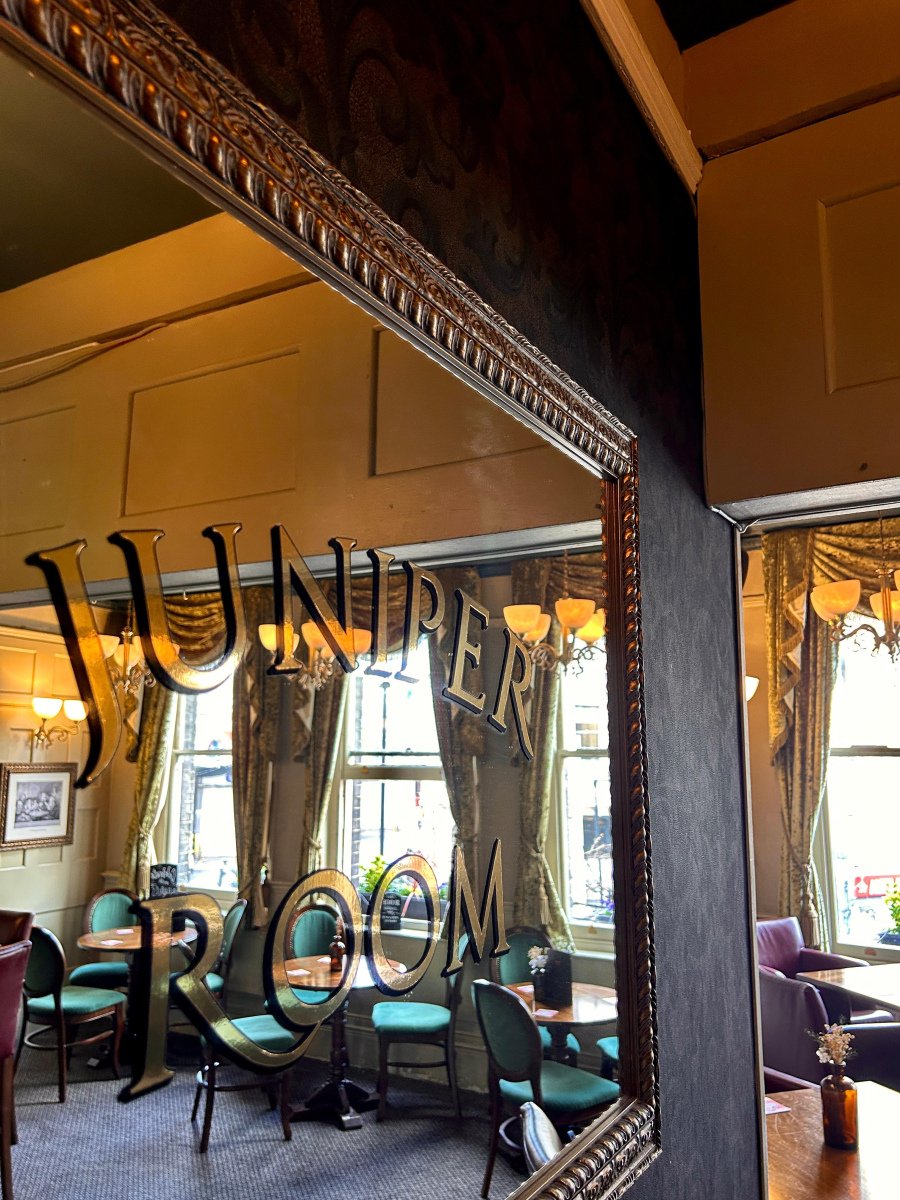 JUNIPER ROOM lettered in gold on an ornate framed mirror, reflecting tables, green chairs and chandeliers