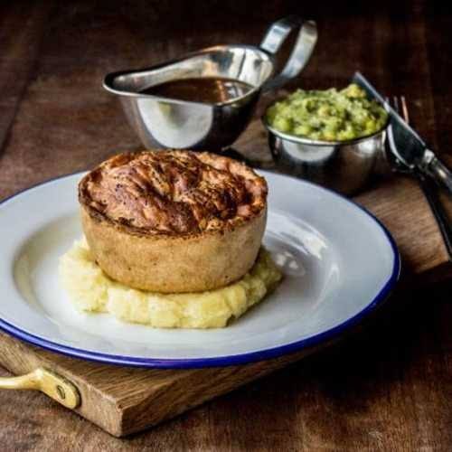 A Pieminister pie on mash, with a jug of gravy and a pot of mushy peas