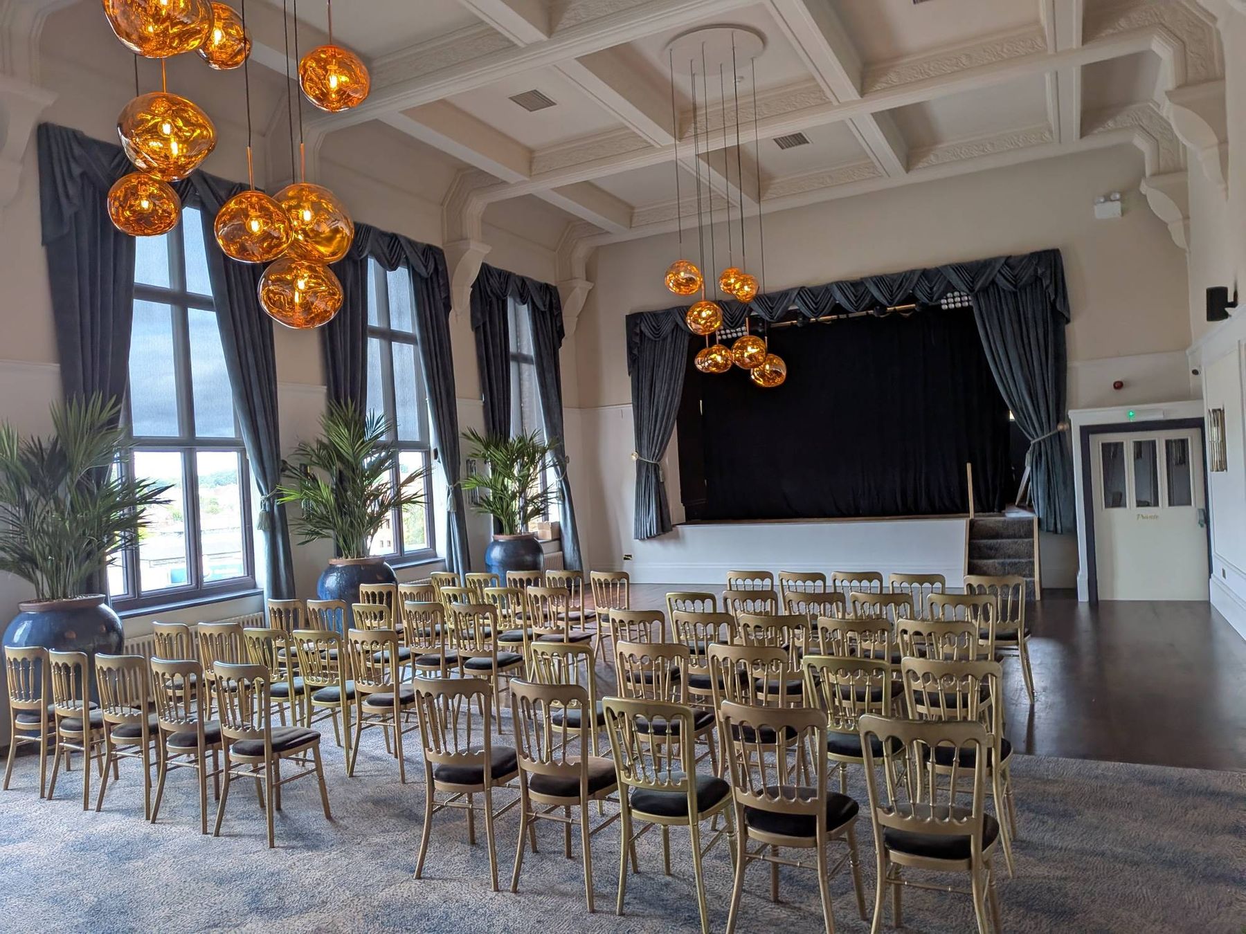 The Grand Suite set for a ceremony: rows of gold chairs facing the stage, tall windows and palms down one side