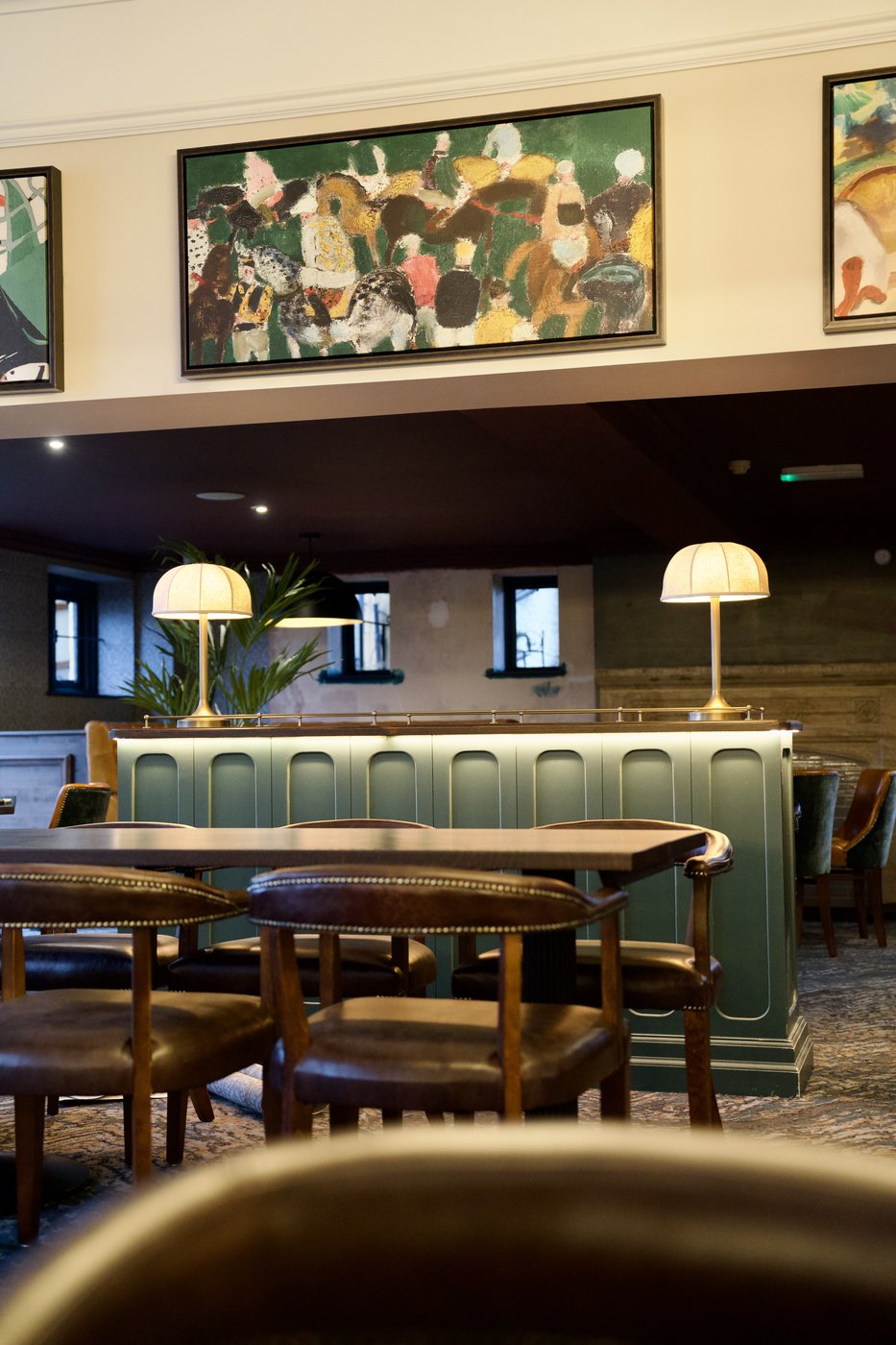 The dining room at The New Inn: a green paneled bar with brass table lamps, dark wood tables and chairs, and framed artwork above