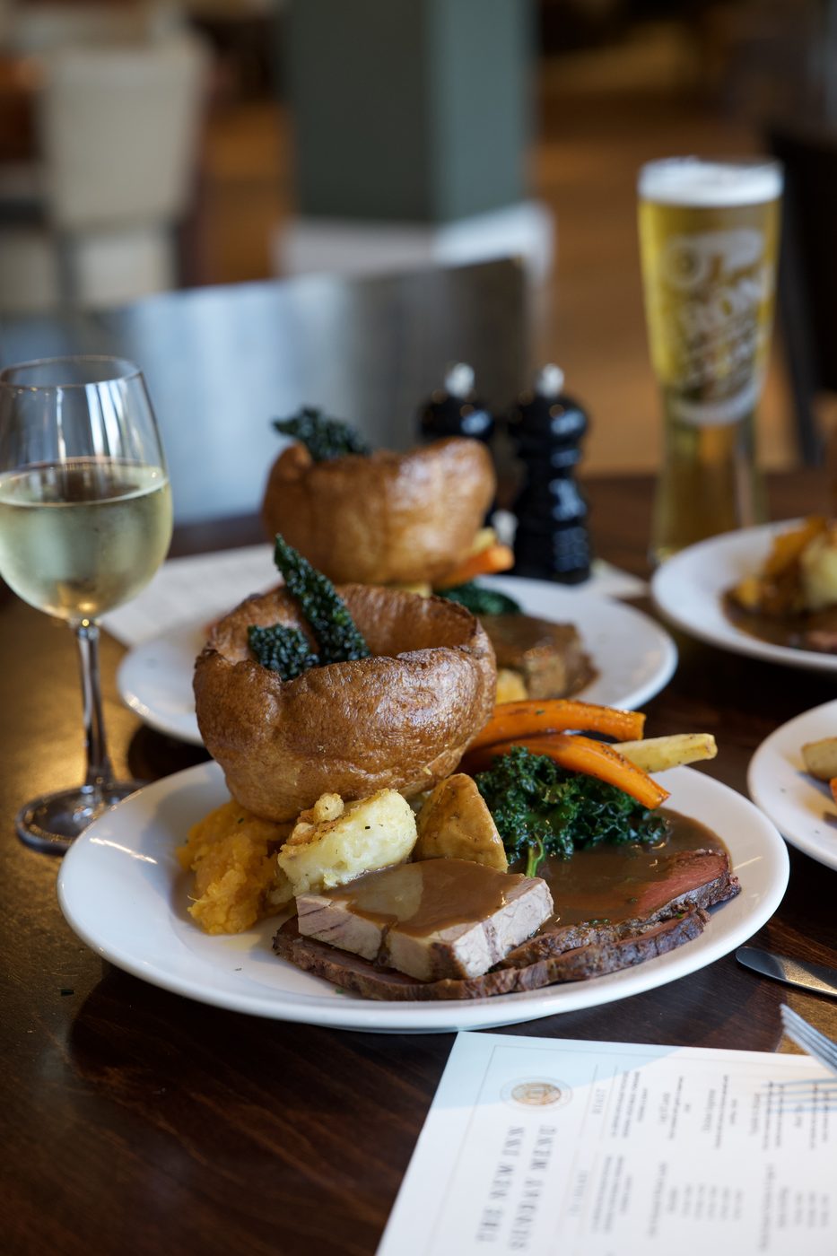 A Sunday roast at The New Inn: sliced beef and pork with a Yorkshire pudding, roast potatoes, carrots, parsnips, kale and gravy, with a glass of wine and a pint alongside