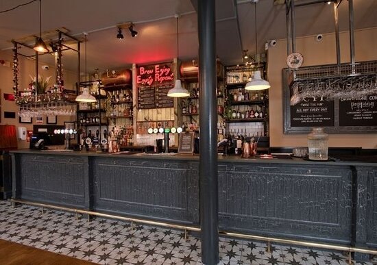 The long bar: black panelled counter on a patterned tiled floor, a red neon sign and shelves of spirits behind