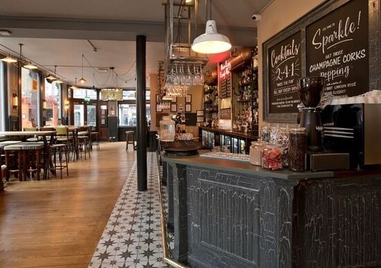 High tables and stools by the windows, with a chalkboard of cocktail offers above the end of the bar