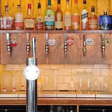 Beer taps on a copper panel below shelves of spirits at the back bar
