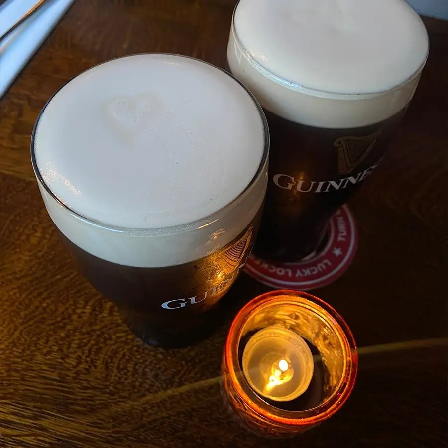 Two pints of Guinness on a wooden table beside a lit candle