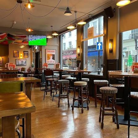 High tables and striped stools by tall windows, bunting overhead and football on the screen