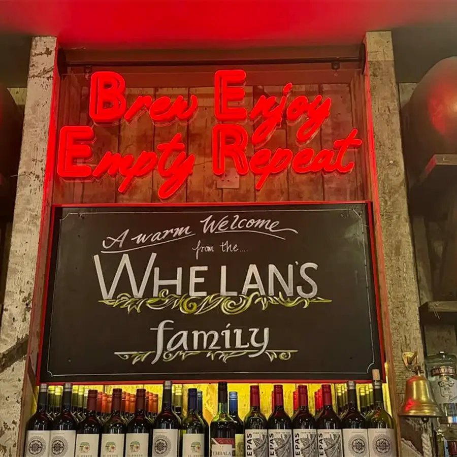 A red neon sign above a chalkboard welcome from the Whelan's family