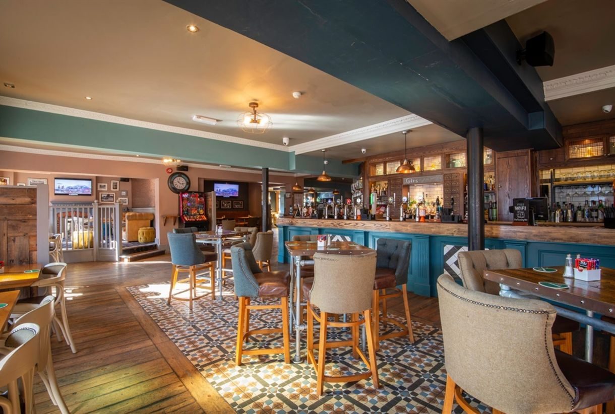 A lounge at The Foundry: a teal bar with leaded-glass cabinets above, wooden tables and a patterned tiled floor