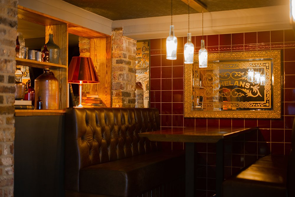 A leather booth beneath a gold-framed Whelans mirror, hanging bottle-shade lights over the table