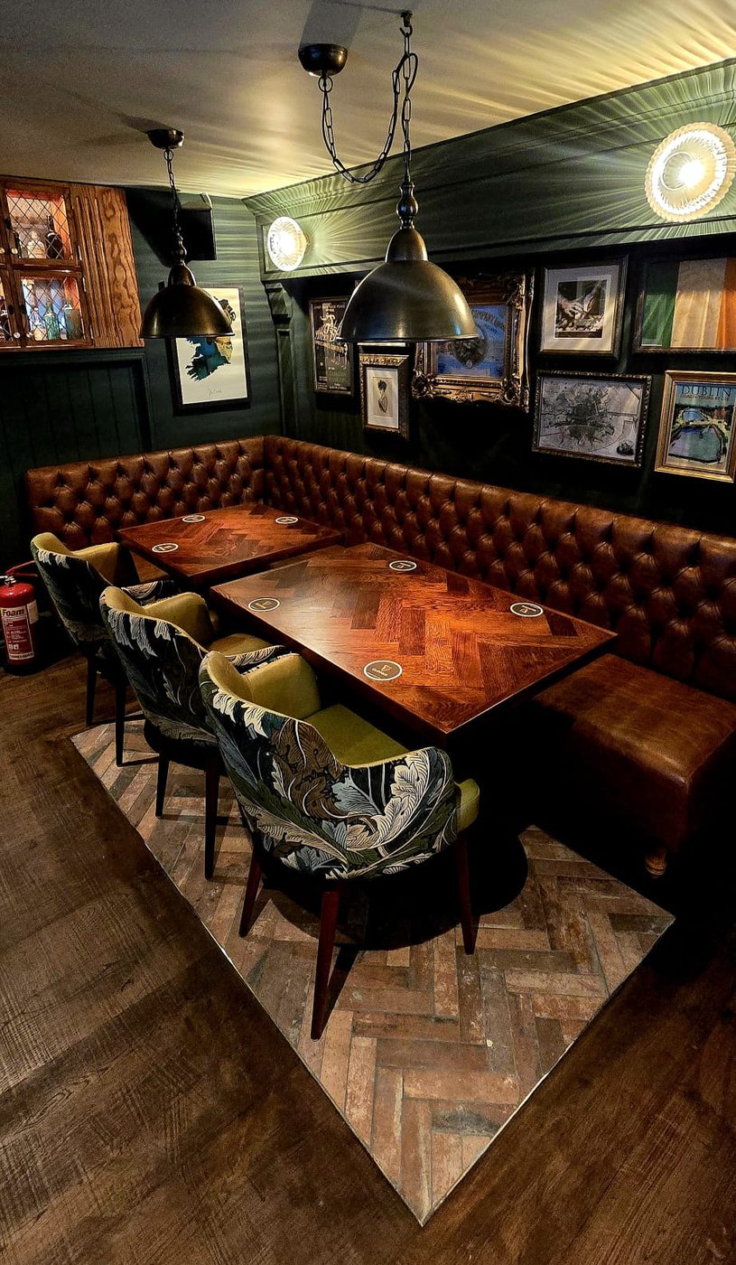 A button-back leather banquette and tables in a dark green room hung with framed pictures