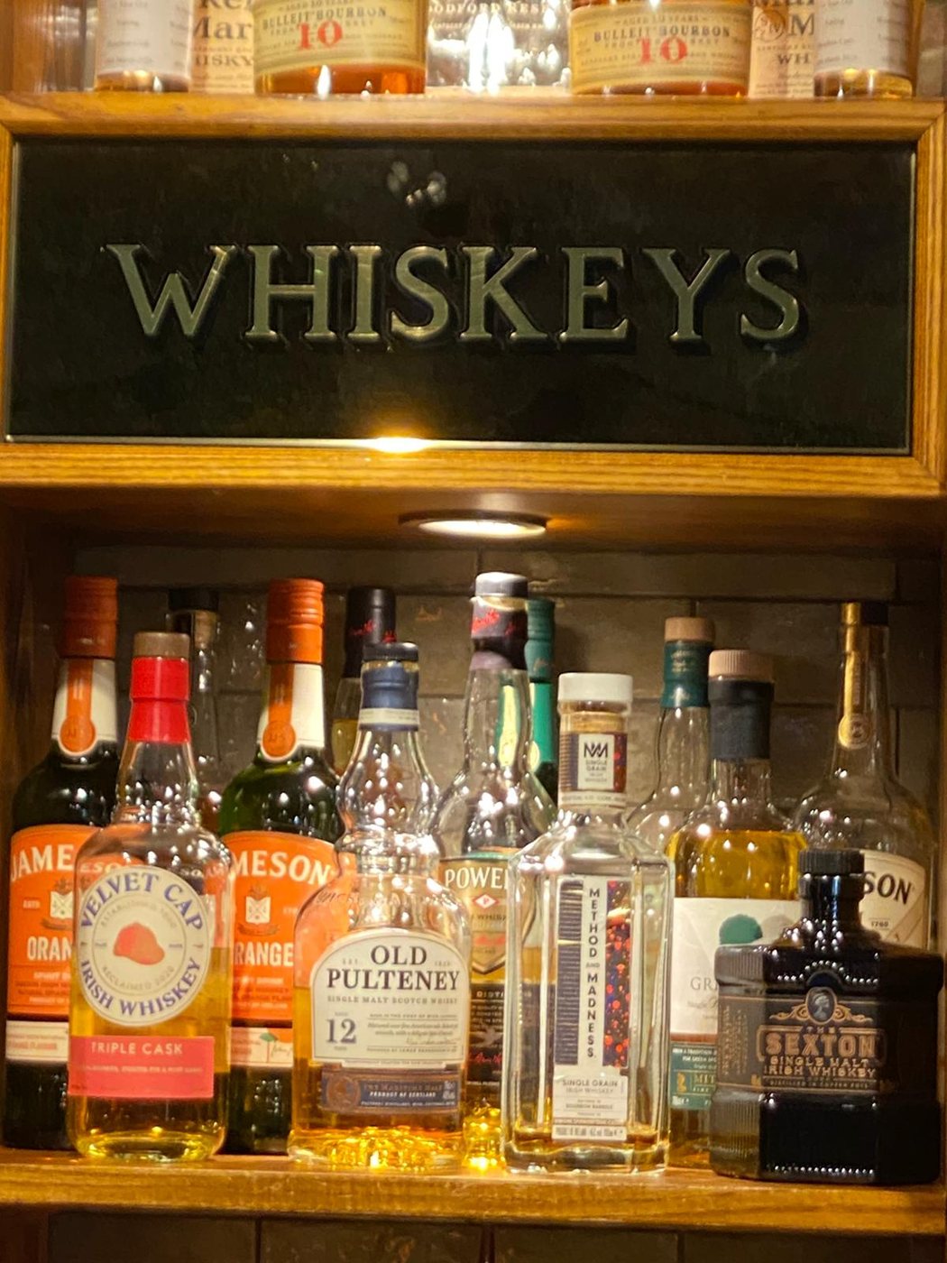 A shelf of whiskeys under a gold-lettered Whiskeys sign